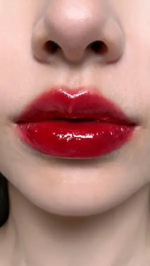 Gros plan sur des lèvres rouges très brillantes sous un nez, avec une texture lisse et un reflet marqué.